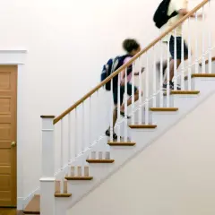 Two people with backpacks ascend a staircase with a new white stair railing and wooden handrail.