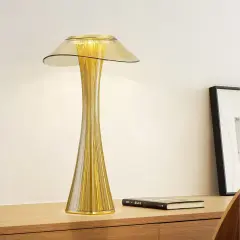 Elegancka, złota lampka stołowa o smukłej, prążkowanej podstawie i szerokim kloszu, tworząca ciepłe światło.