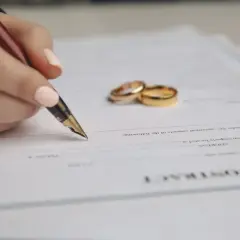 Dłoń z piórem podpisuje dokument, obok leżą obrączki. To umowa o rozdzielność majątkową.
