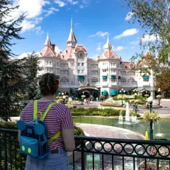 Dziewczyna z plecakiem w kształcie Myszki Miki patrzy na zamek w Disneylandzie. Zastanawia się, ile kosztuje bilet do Disneylandu.