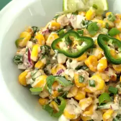 Deliciosa ensalada de maiz cremosa con jalapeños, cebolla morada y cebollín, servida en un tazón blanco.