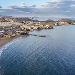 Vista aérea de la costa de Pulpí, con su extensa playa de arena dorada y el mar azul. El pueblo se extiende por la ladera de las colinas.