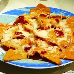 Nachos con queso derretido y salsa roja, servidos en un plato azul y verde. ¡Un antojo irresistible!
