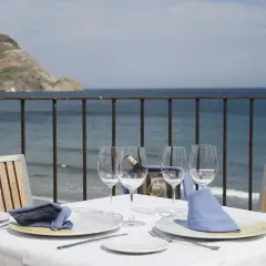 Mesa puesta en Doña Pakyta restaurante con vistas al mar. Copas, platos y servilletas azules esperan a los comensales.