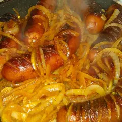 Gorąca kiełbasa z cebulą skwierczy na patelni, tworząc apetyczny aromat.