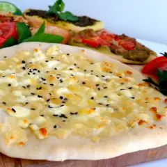 Manakish recept: Färsk ost och svarta sesamfrön på en tunn botten, med andra varianter i bakgrunden.