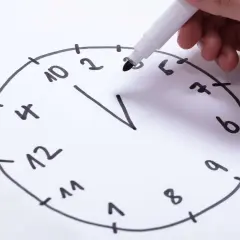 Hand zeichnet eine Uhr für einen Uhrentest Demenz. Die Zahlen sind unvollständig und die Zeiger fehlen.