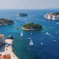 Un día perfecto para tu ruta Croacia 7 días: veleros navegan en aguas turquesas cerca de islas verdes y la histórica ciudad amurallada.