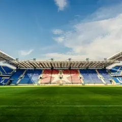 Pusta trybuna stadionu Wisły Kraków, z niebieskimi i czerwonymi siedzeniami tworzącymi wzór gwiazdy. Pojemność stadionu robi wrażenie.