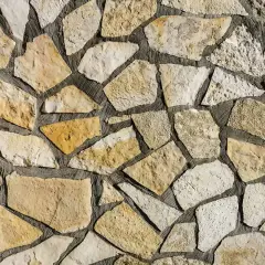 Kamienna ściana z nieregularnych, żółtawych i białych kamieni. Piaskowiec tworzy naturalną, rustykalną mozaikę.