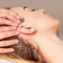 Mains douces appliquant une thérapie cranio sacrée sur la tête d'une femme détendue.