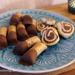 Mandelstangen mit Marzipan und schokoladenüberzogenen Keksen auf blauem Teller.