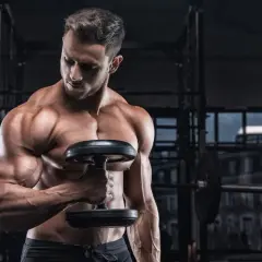 Uomo muscoloso in palestra con manubrio, focus sulla definizione muscolare, integrando la creatina per massimizzare i risultati.