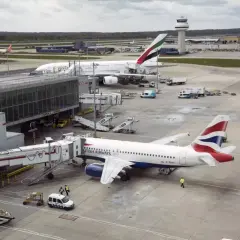 Samoloty British Airways i Emirates na lotniskach w Londynie. W tle wieża kontroli lotów.
