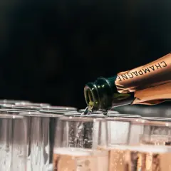 Versando champagne da una bottiglia in una fila di bicchieri, mostrando diversi tipi di champagne.