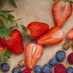 Frische Erdbeeren, Blaubeeren und Himbeeren liegen bereit, um sie einzufrieren. Ein paar Haselnüsse und grünes Blattwerk runden das Bild ab.