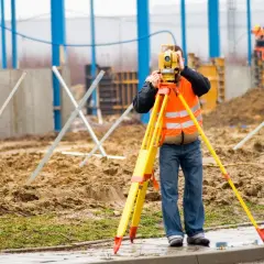Geodeta w kamizelce odblaskowej mierzy teren za pomocą niwelatora na budowie.