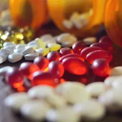 Mnóstwo tabletek i kapsułek, w tym czerwone, białe i żółte, rozsypanych wokół pomarańczowych pojemników. To może być zapas leków, w tym antybiotyków.