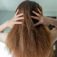 Manos revolviendo el pelo encrespado de una mujer, mostrando la textura seca y desordenada.