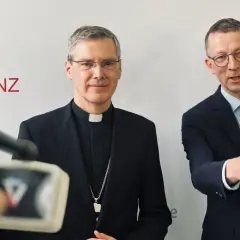 Der Vorsitzende der Deutschen Bischofskonferenz, Georg Bätzing, im Gespräch mit einem Mann im Anzug.