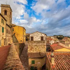 Un vicolo con case gialle e un campanile a Montescudaio. Tetti rossi e cielo nuvoloso, un'atmosfera suggestiva per scoprire cosa vedere.