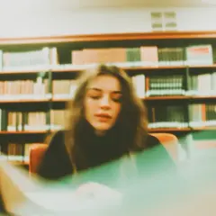 Młoda kobieta pochylona nad laptopem w bibliotece, otoczona regałami pełnymi książek. Tworzy swoją bibliografię.