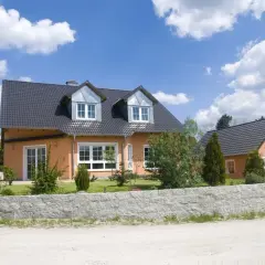 Pomarańczowy dom z szarym dachem, dawny budynek gospodarczy, teraz przekształcony na mieszkalny, z zielonym ogrodem i kamiennym murem.