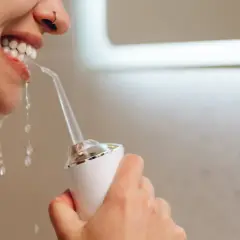 Kobieta pokazuje, jak używać irygator do zębów, strumień wody płucze jej zęby.
