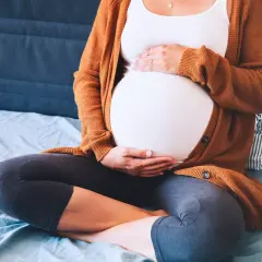 Mujer embarazada sentada, con las manos sobre su vientre. Ejercicios para el embarazo y alivio de la pubalgia.