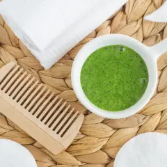 Un tazón con **te verde para el pelo**, un peine de madera, toallas blancas y discos de algodón sobre una estera tejida.