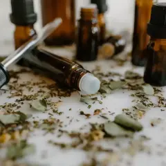 Butelki z ciemnego szkła, pipeta i rollerball otoczone suszonymi ziołami. To może być zestaw do tworzenia własnych olejków, które można aplikować jak vaporisateur spray.