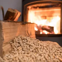 Drewno i pellet z trocin przed palącym się kominkiem. Tak się robi pellet z trocin, ekologiczne paliwo.