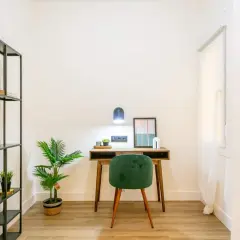 Escritorio con silla verde, planta y estantería. La lámpara regulable intensidad ilumina el espacio de trabajo.