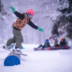 Dziecko na snowboardzie balansuje na rurze w spindleruv mlyn snowpark. W tle inni snowboardziści.