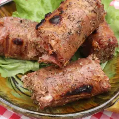 Trois andouillettes grillées au barbecue, servies sur un lit de laitue dans une assiette décorative.