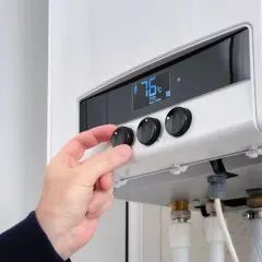 Hand dreht Regler an Heizung. 76°C. Was bedeutet 65 Prozent erneuerbare Energien? Effizienz ist wichtig.