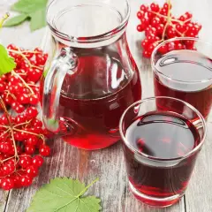 Kielichy i dzbanek wypełnione czerwonym sokiem z kaliny. Obok kiście świeżych owoców kaliny i liście.