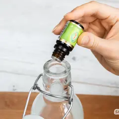 Eine Hand tropft ätherisches Öl in eine Glasflasche, um Mundwasser selber zu machen.