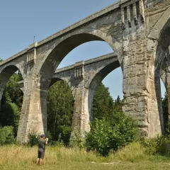 Imponujące mosty w Stańczykach, zbudowane z kamienia, górują nad zielonym krajobrazem. Mężczyzna z aparatem dokumentuje ich monumentalność.