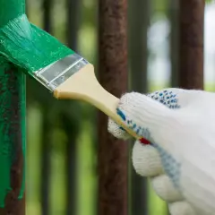 Mano guantata stende vernice verde su un palo di ferro arrugginito. La temperatura ideale per verniciare il ferro è fondamentale per una buona resa.