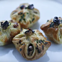 Cztery apetyczne paczuszki z ciasta francuskiego z gruszkami i gorgonzolą, posypane ziołami.