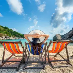 Kobieta w kapeluszu odpoczywa na leżaku na tropikalnej plaży.