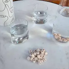 Des perles de céramique dans une carafe d'eau pour purifier l'eau du robinet naturellement. Des verres d'eau et un pichet décoratif complètent la scène.