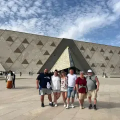 Rodzina pozuje przed nowoczesnym, geometrycznym budynkiem – nowym muzeum w Egipcie.