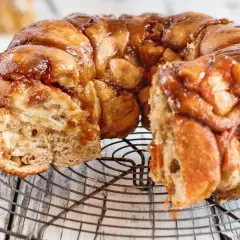 Pyszny, karmelizowany monkey bread przepis na okrągłej kratce. Ciasto jest lekko rozwarstwione, z widocznymi kawałkami ciasta.