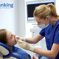 Dentystka w maseczce bada zęby pacjentki w gabinecie stomatologicznym.