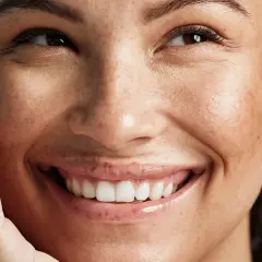 En närbild av en kvinna med fräknar som ler. Hennes hud ser naturlig och frisk ut, en inspiration för hur blir man en clean girl.
