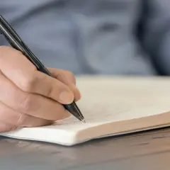Hand schreibt mit einem Stift in ein Notizbuch. Wichtige Details für das protokoll schreiben festhalten.