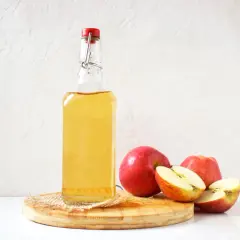 Butelka z płynnym złotym płynem, obok jabłka. Czy to naturalne wsparcie dla kobiet w ciąży? Ocet jabłkowy w ciąży może być pomocny.