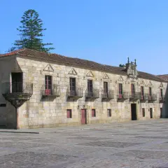 El Pazo de Fefiñanes, un edificio de piedra con balcones de hierro forjado, se alza bajo un cielo azul.